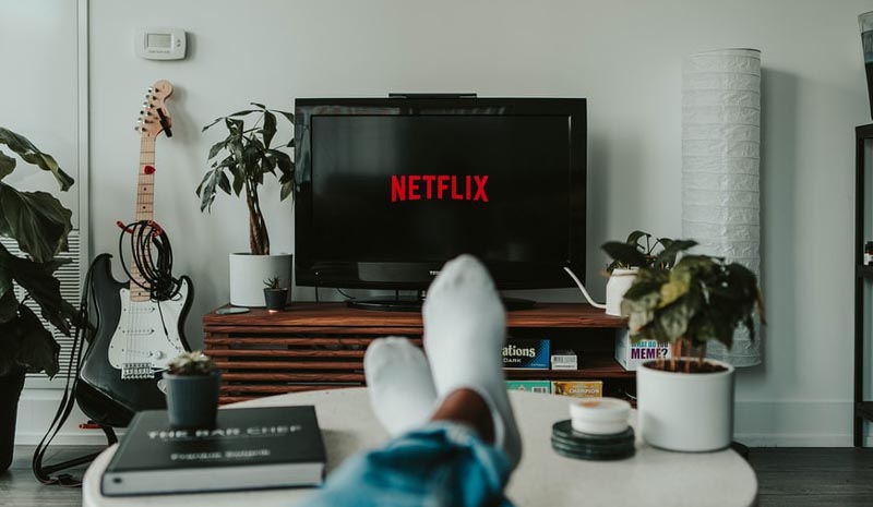 Una persona descansa en su living mientras enciende Netflix en su televisor.