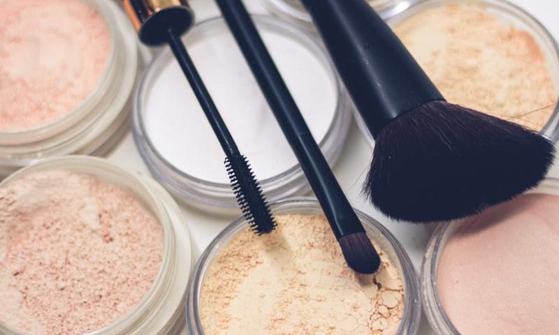 Foto de brochas y pinceles sobre polvos de maquillaje en tonos rosados y nude