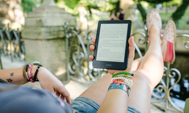 Persona recostada con las piernas estiradas leyendo de un ebook-reader