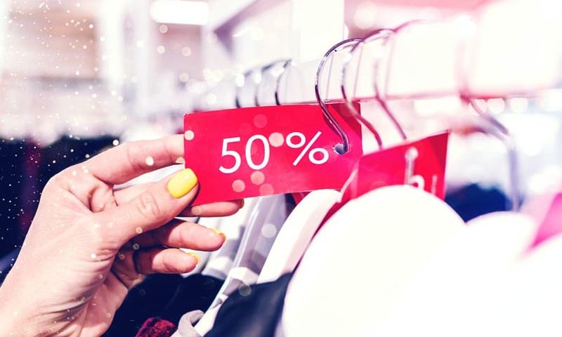 Mujer mira etiqueta de 50% de descuento en el perchero de un local