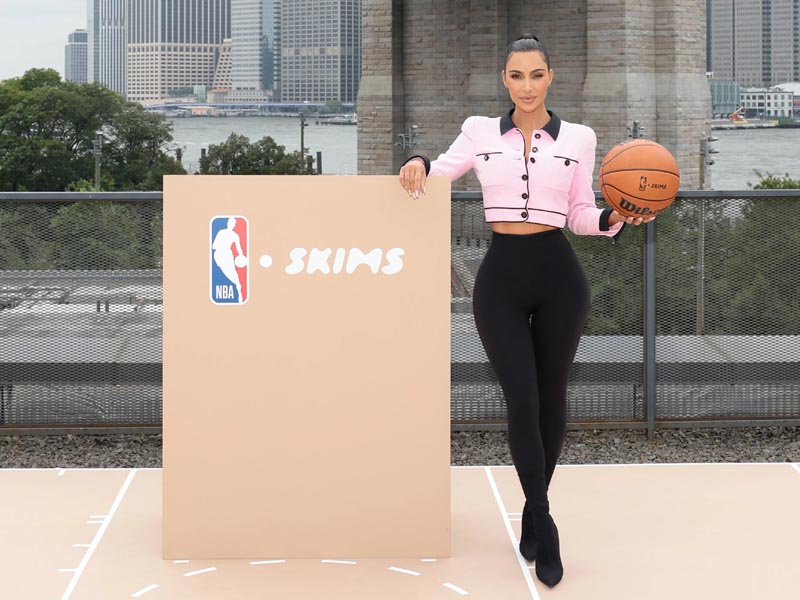 Kim Kardashian con una pelota de basket en un estrado de la NBA y su marca SKIMS