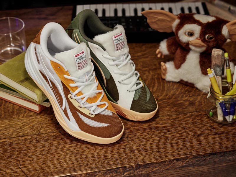 zapatillas de PUMA x GREMLINS Collection sobre un escritorio de madera, junto a un muñeco de Gizmo y un vaso de agua