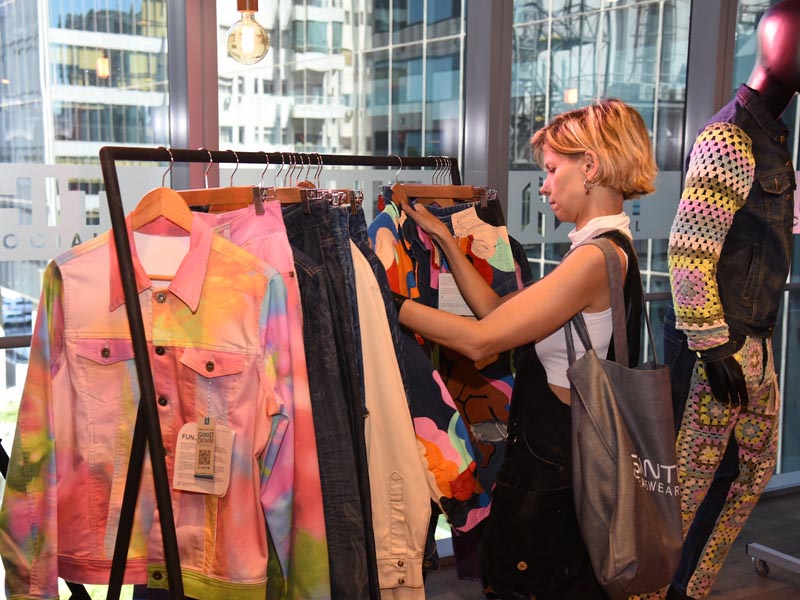 Una mujer mira prendas colgadas de denim y gabardina de colores en un perchero en el evento de presentación de Inconecting SS 2025 de Santista