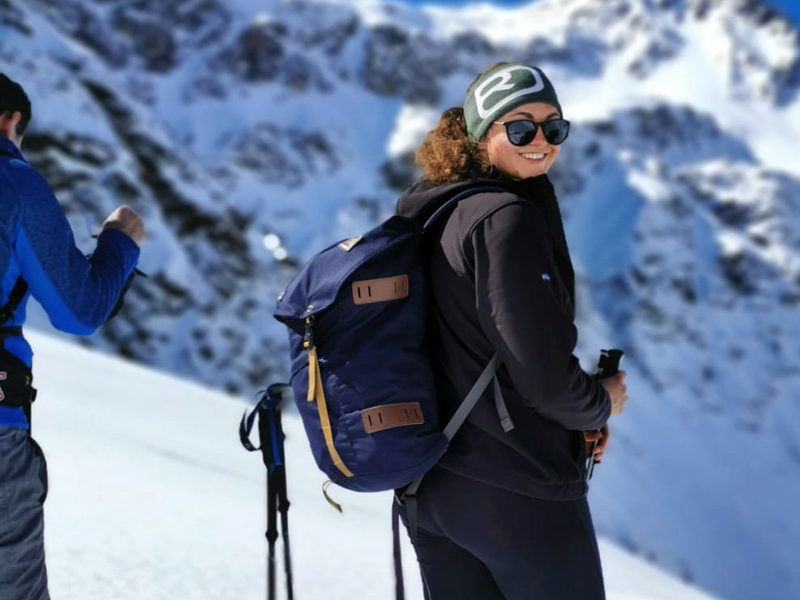 Mujer en la montaña nevada con gorro, anteojos de sol y skies puestos